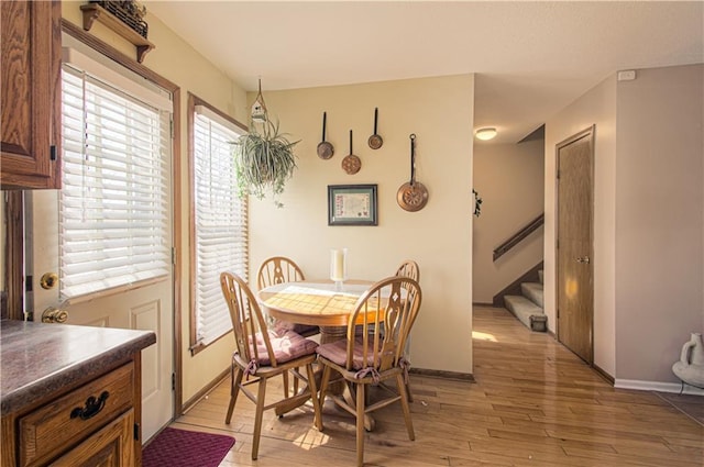 dining room with light wood-type flooring, a healthy amount of sunlight, baseboards, and stairs