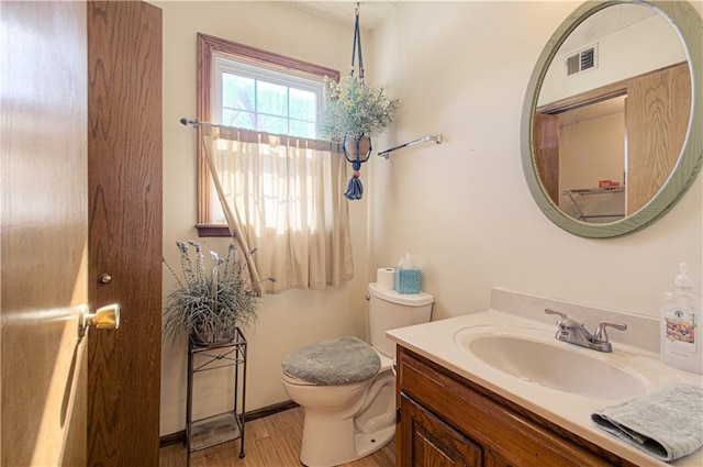 half bath with visible vents, vanity, toilet, and wood finished floors