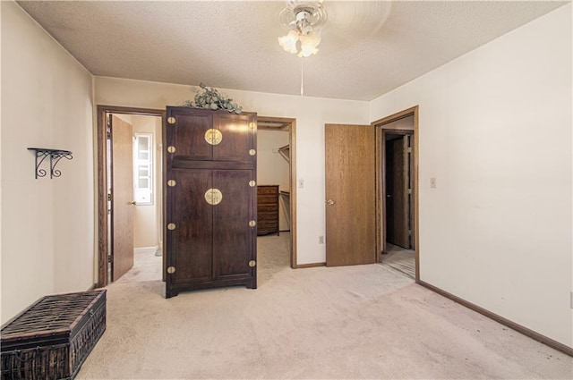 bedroom with a walk in closet, light colored carpet, a textured ceiling, and baseboards