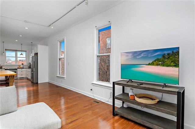 living area featuring baseboards, visible vents, ornamental molding, wood finished floors, and track lighting