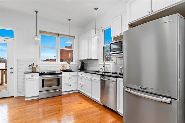 kitchen featuring stainless steel appliances, dark countertops, a sink, and decorative light fixtures