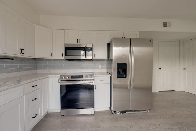 kitchen featuring light stone counters, stainless steel appliances, visible vents, white cabinets, and backsplash