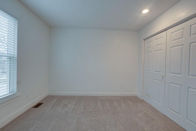 unfurnished bedroom with light carpet, baseboards, multiple windows, and visible vents