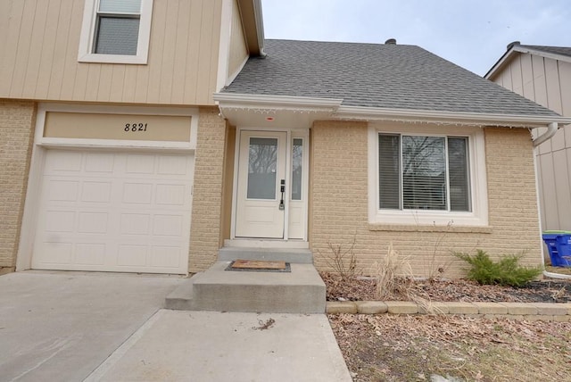 property entrance with concrete driveway, a shingled roof, and brick siding