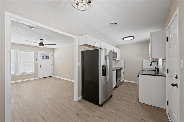 kitchen with sink, appliances with stainless steel finishes, white cabinetry, tasteful backsplash, and light wood-type flooring