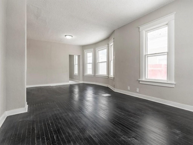 unfurnished room featuring plenty of natural light, dark wood-type flooring, and a textured ceiling