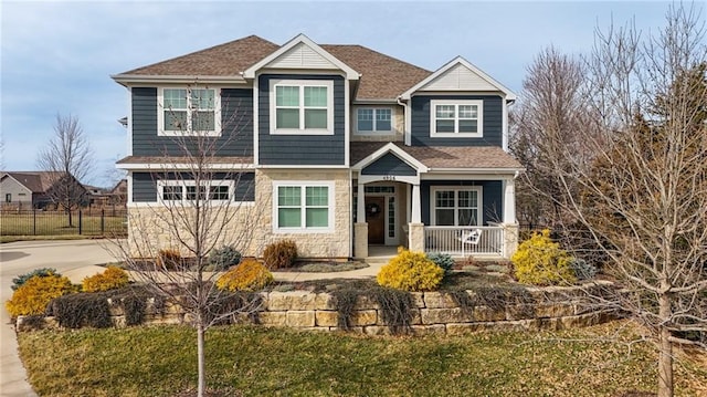 craftsman-style home with driveway, a shingled roof, stone siding, covered porch, and fence