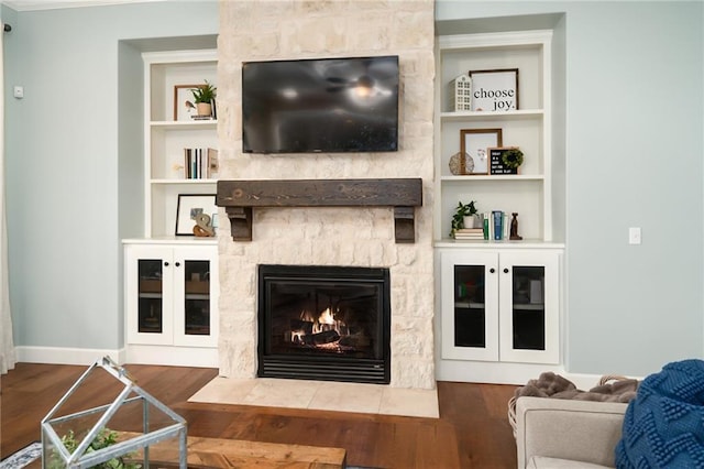living area featuring baseboards, built in features, wood finished floors, and a fireplace