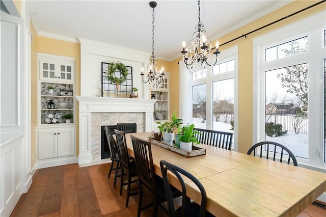 dining space featuring crown molding, dark wood finished floors, a tiled fireplace, and an inviting chandelier