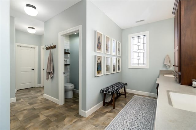 bathroom featuring a sink, double vanity, toilet, baseboards, and visible vents