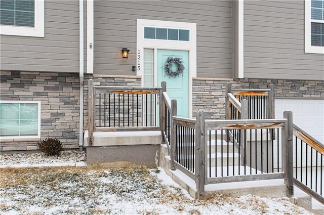 snow covered property entrance with an attached garage and stone siding