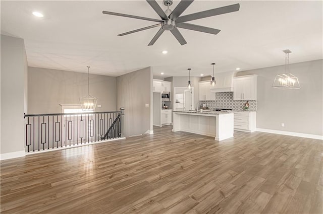 unfurnished living room featuring baseboards, ceiling fan with notable chandelier, wood finished floors, and recessed lighting