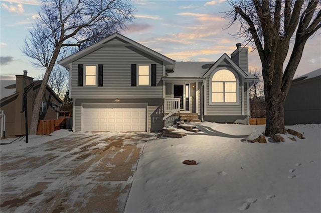 tri-level home featuring fence, a garage, driveway, and a chimney