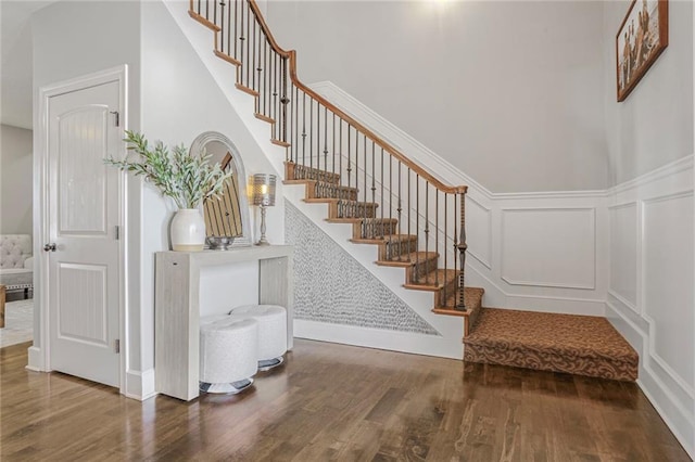 stairs with a wainscoted wall, a high ceiling, a decorative wall, and wood finished floors