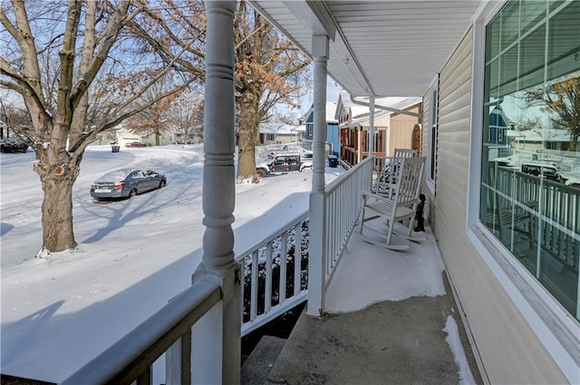 snow covered back of property featuring covered porch