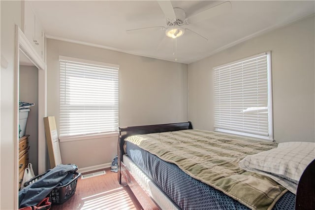 bedroom with ceiling fan, wood finished floors, visible vents, and baseboards