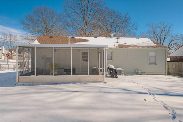 snow covered rear of property with a sunroom and fence