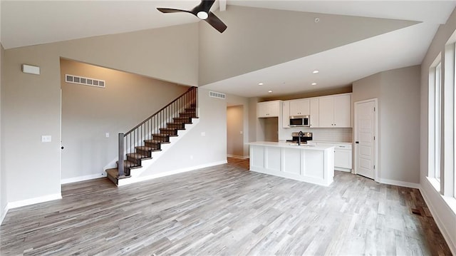 interior space with a center island with sink, light hardwood / wood-style floors, sink, ceiling fan, and white cabinets