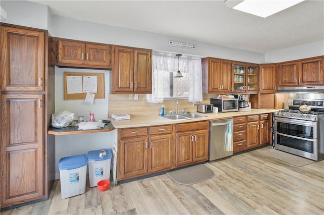 kitchen featuring stainless steel appliances, pendant lighting, sink, and light hardwood / wood-style floors