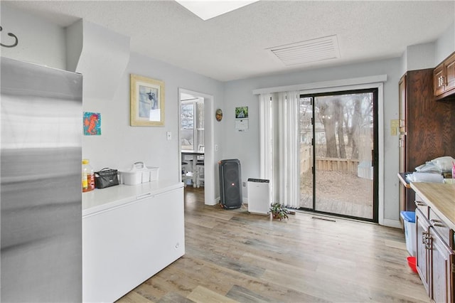 kitchen with stainless steel fridge, a textured ceiling, light wood-type flooring, and refrigerator