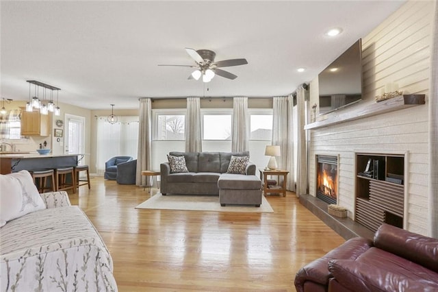 living room featuring ceiling fan, a glass covered fireplace, light wood-style flooring, and a healthy amount of sunlight