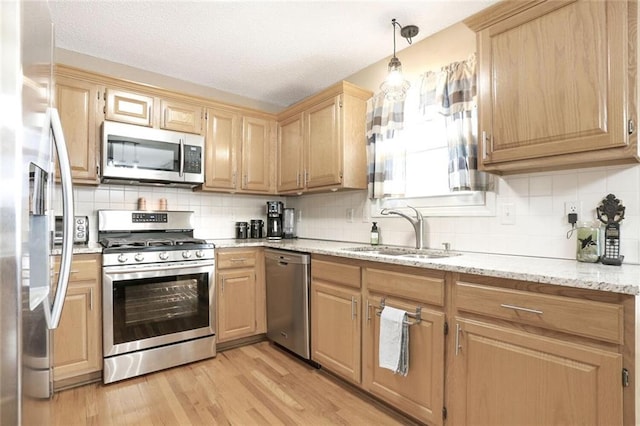 kitchen with light wood finished floors, appliances with stainless steel finishes, light stone counters, light brown cabinetry, and a sink