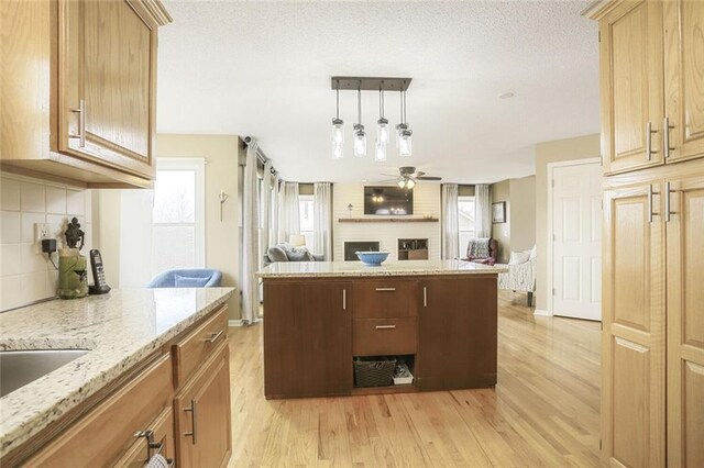 kitchen featuring ceiling fan, open floor plan, light wood-style floors, a fireplace, and backsplash