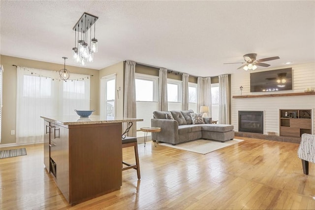 interior space featuring light wood-style flooring, a fireplace, a ceiling fan, and a textured ceiling