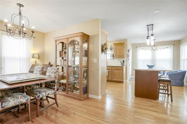 dining room with a chandelier, baseboards, a textured ceiling, and light wood finished floors