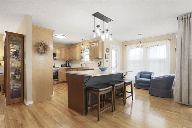 kitchen with stainless steel appliances, a healthy amount of sunlight, light brown cabinets, light wood-type flooring, and a kitchen breakfast bar