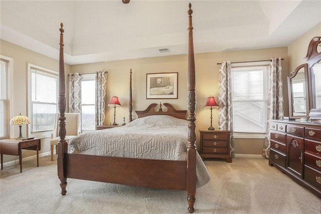 bedroom with a tray ceiling, light colored carpet, visible vents, and baseboards