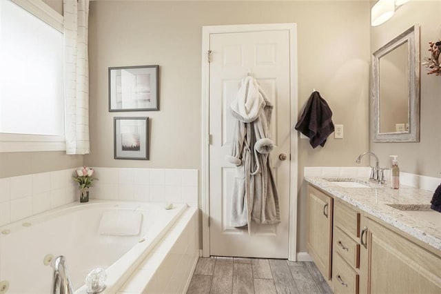 bathroom with double vanity, a garden tub, a sink, and wood finished floors