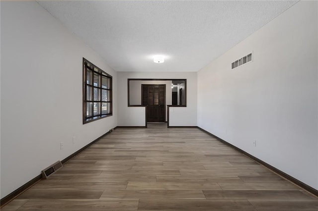 empty room featuring baseboards, a textured ceiling, visible vents, and wood finished floors