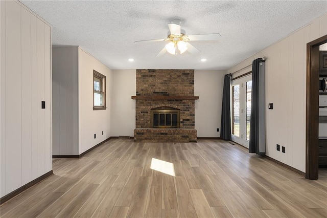 unfurnished living room featuring a textured ceiling, light wood-type flooring, a ceiling fan, and a brick fireplace