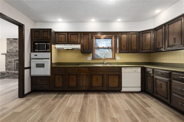 kitchen with light wood finished floors, white appliances, a sink, and under cabinet range hood