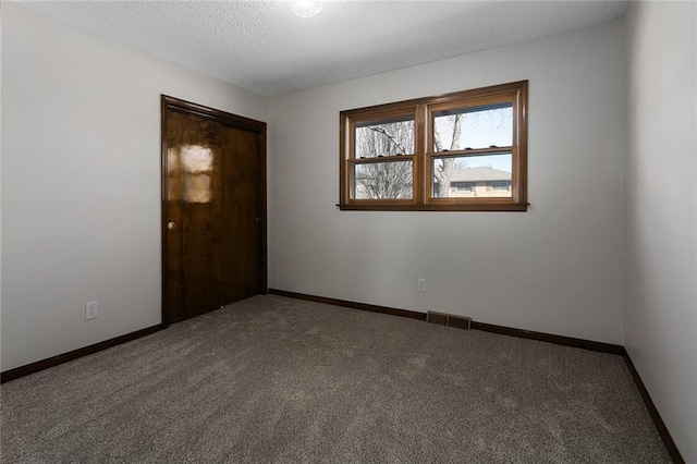 spare room featuring carpet, visible vents, a textured ceiling, and baseboards