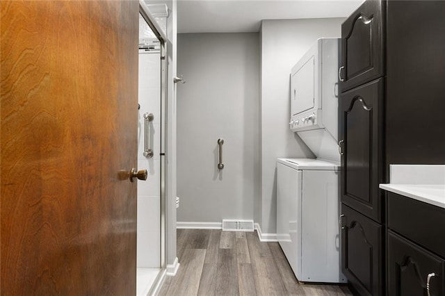 washroom featuring wood finished floors, visible vents, baseboards, stacked washing maching and dryer, and cabinet space