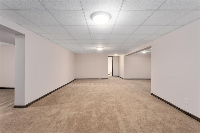 finished basement with carpet floors, baseboards, and a paneled ceiling