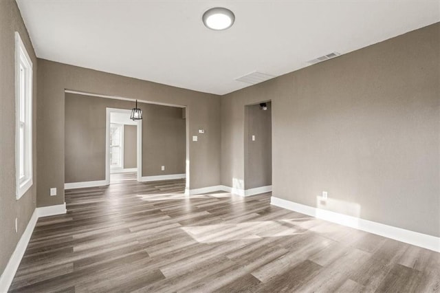 empty room with wood finished floors, visible vents, and baseboards