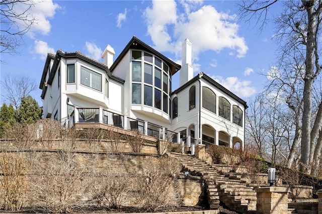 back of house featuring stairs, a sunroom, and stucco siding