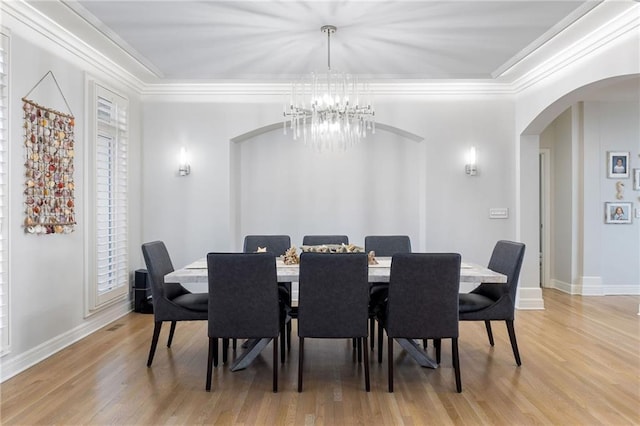 dining area featuring crown molding, baseboards, a chandelier, light wood-style floors, and arched walkways