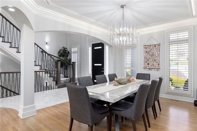 dining room with stairway, arched walkways, light wood-style flooring, and crown molding