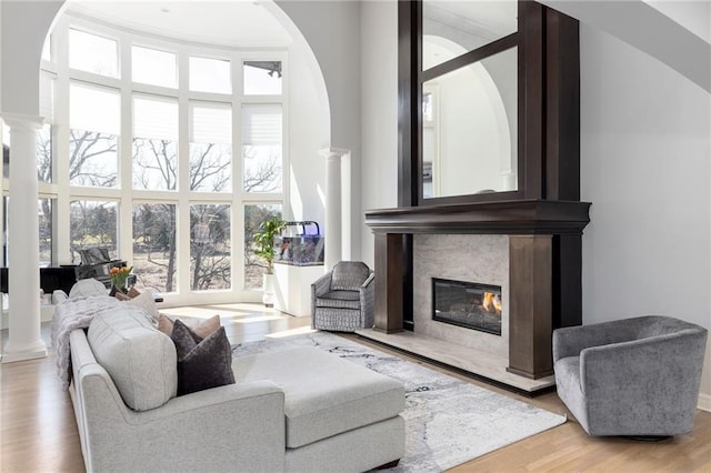 living room featuring a high end fireplace, arched walkways, ornate columns, and wood finished floors