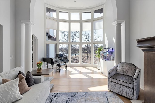 living room featuring arched walkways, a high ceiling, ornate columns, and wood finished floors