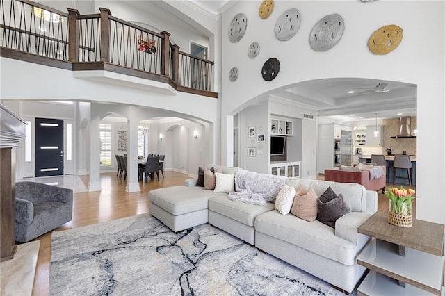 living room with crown molding, ceiling fan, a towering ceiling, wood finished floors, and arched walkways