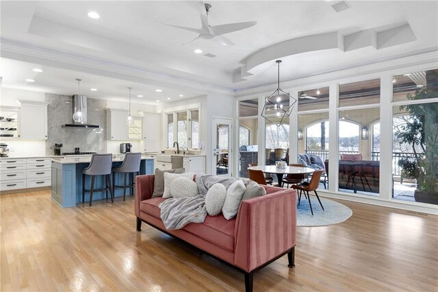 living room with a tray ceiling, plenty of natural light, light wood-style floors, and a ceiling fan