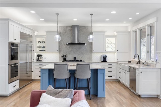 kitchen featuring stainless steel appliances, wall chimney exhaust hood, and white cabinetry