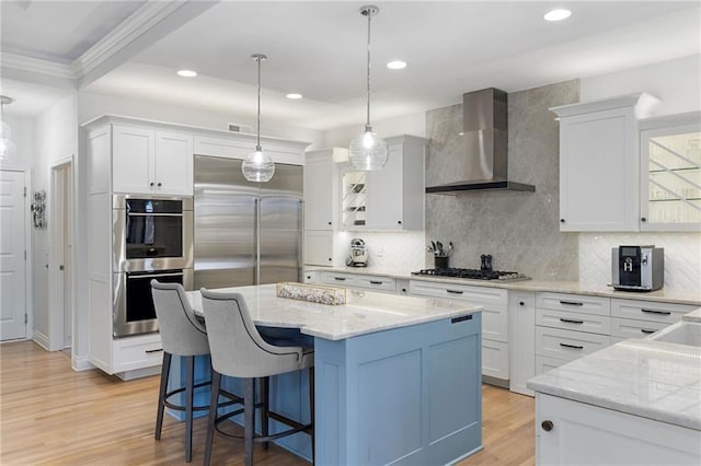 kitchen featuring white cabinets, appliances with stainless steel finishes, wall chimney exhaust hood, and light wood-style floors