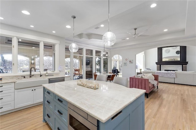 kitchen with arched walkways, a sink, white cabinets, a raised ceiling, and stainless steel microwave