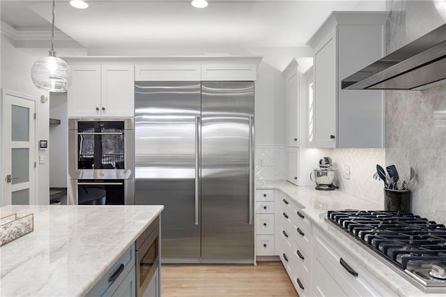 kitchen featuring light wood-type flooring, built in appliances, wall chimney exhaust hood, and light stone countertops